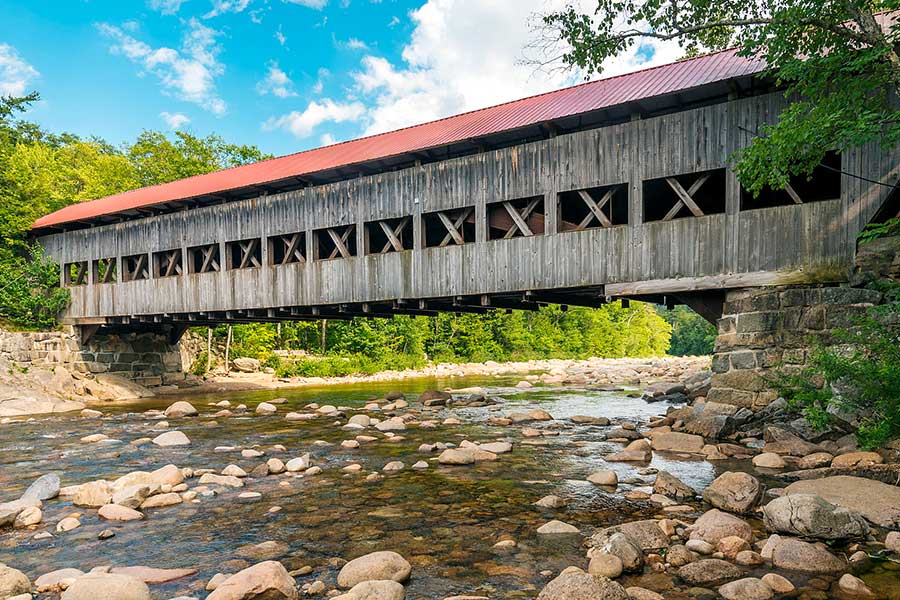 Wooden covered bridge with red roof crossing stream