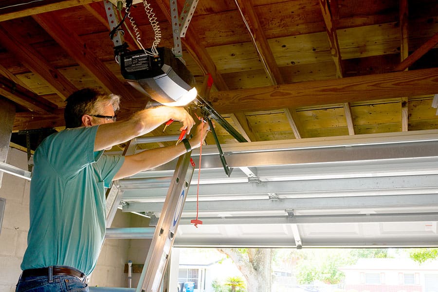 Man on ladder installing garage door opener
