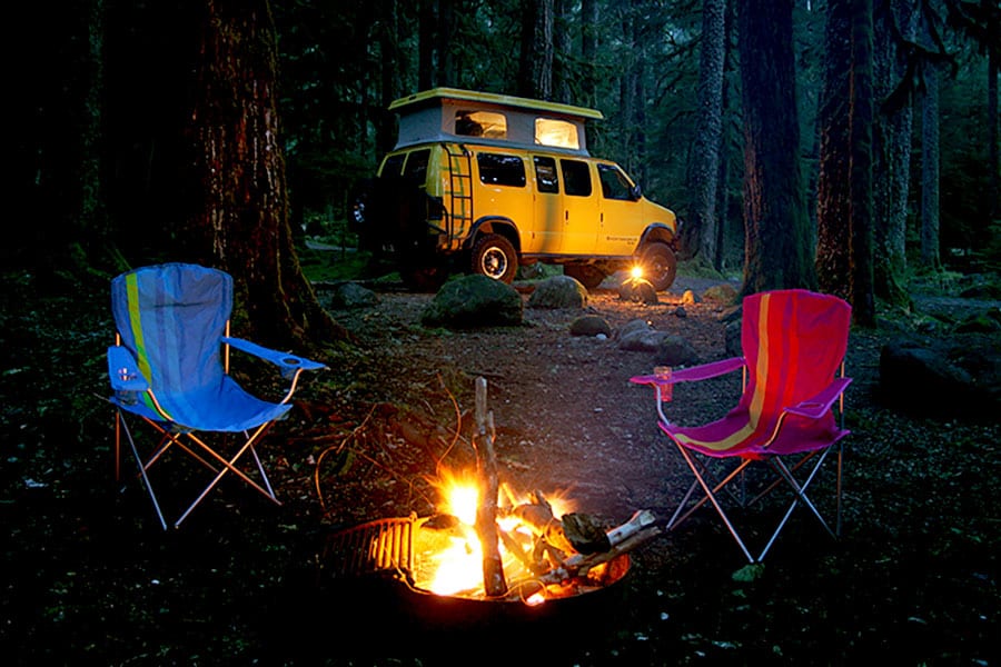 Night camping scene with van, fire and camping chairs
