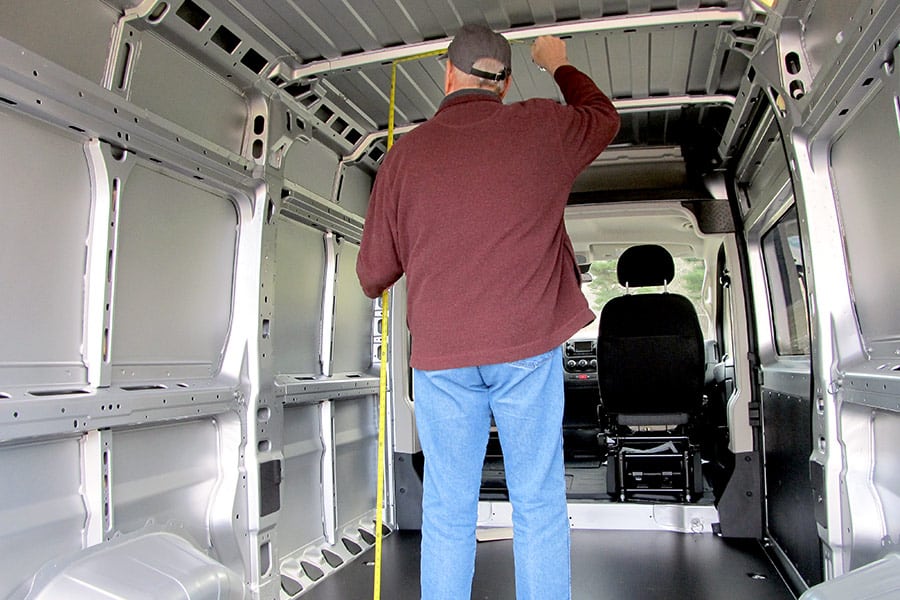 Man standing in the cargo area of a van measuring the height