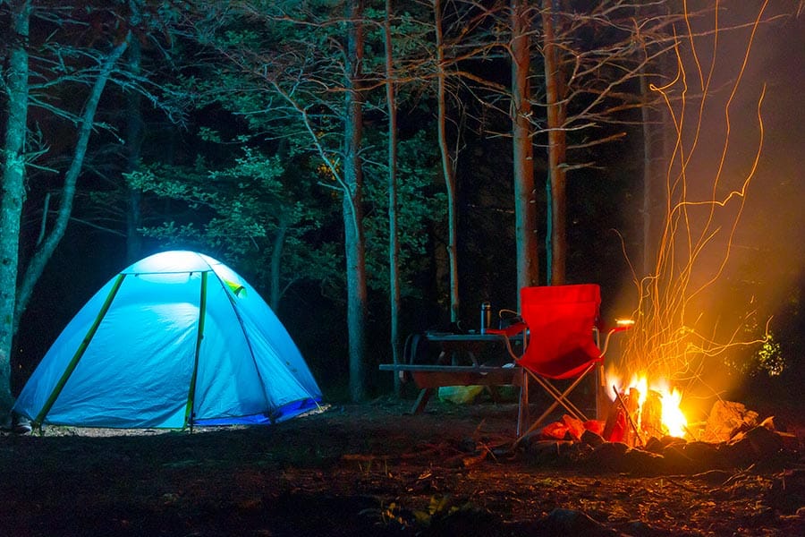 Illuminated blue tent pitched beside a campfire