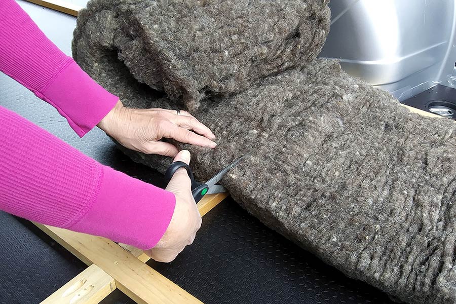 Woman cutting wool insulation on the floor of a van