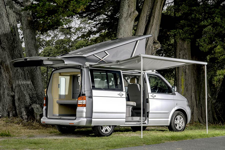 Silver van with awning extended and doors open parked in the woods