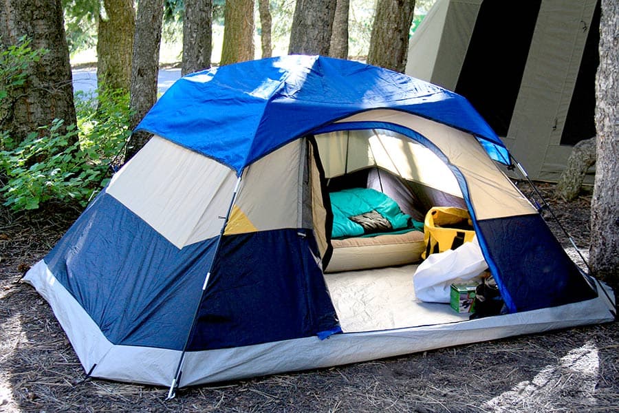 Blue and white tent with bedding inside in a wooded area