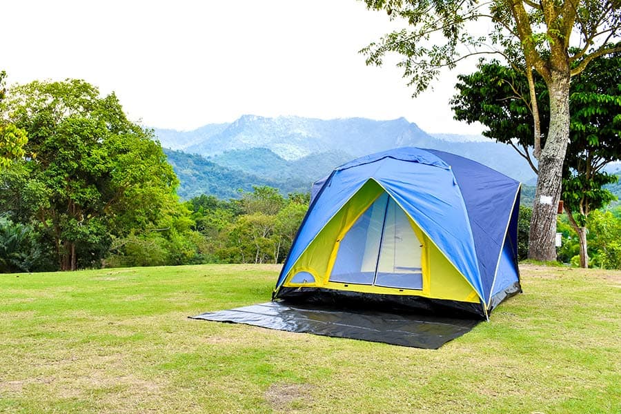 Blue and yellow tent with a ground sheet pitched on grass with mountains in the background