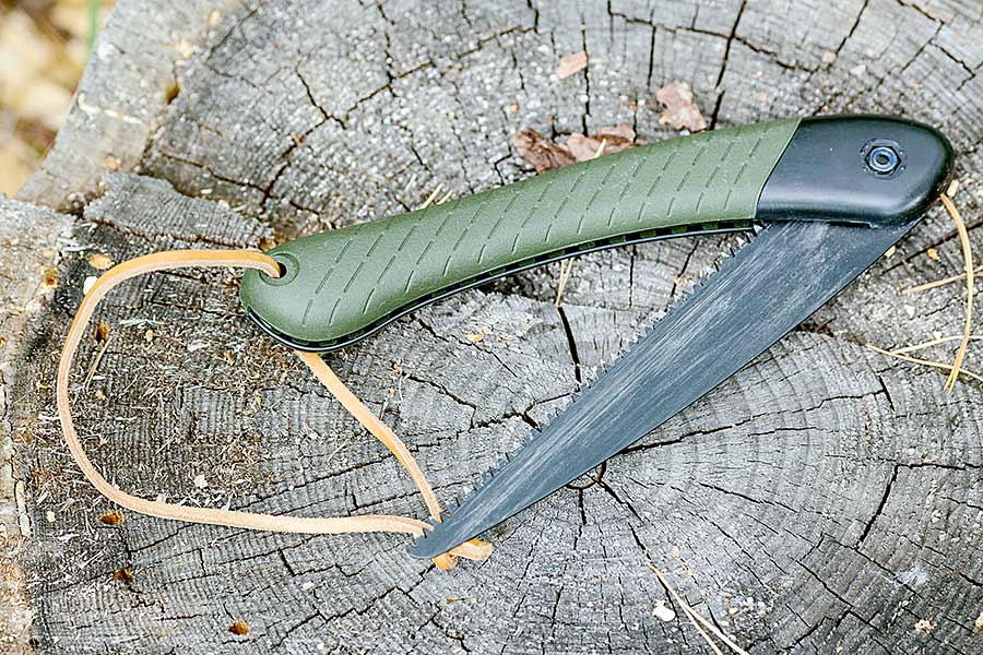 Green folding camp saw on a piece of wood