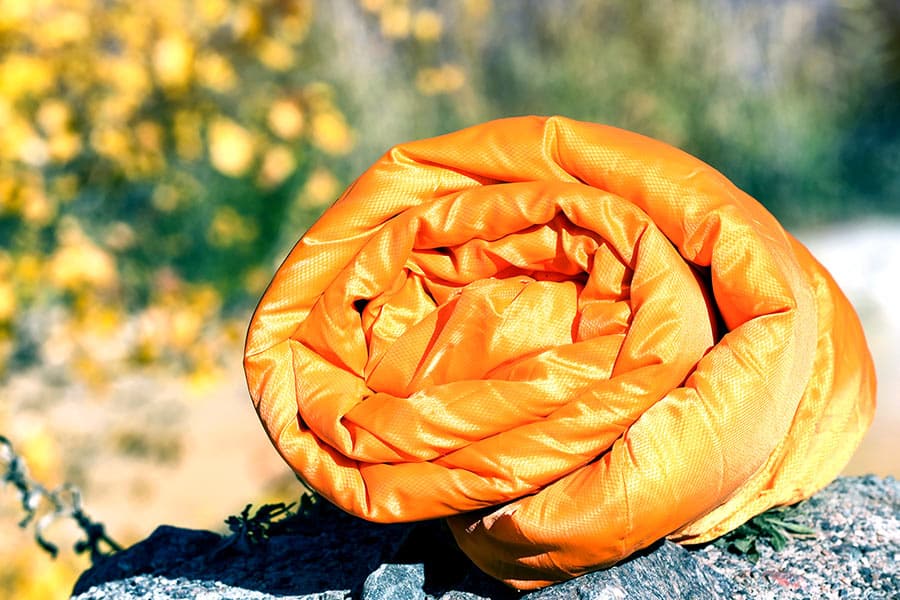 Orange sleeping bag rolled up on ground
