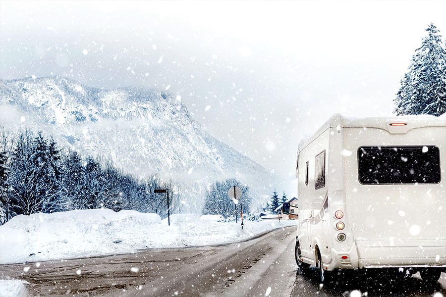A RV on the road going through snowy mountains