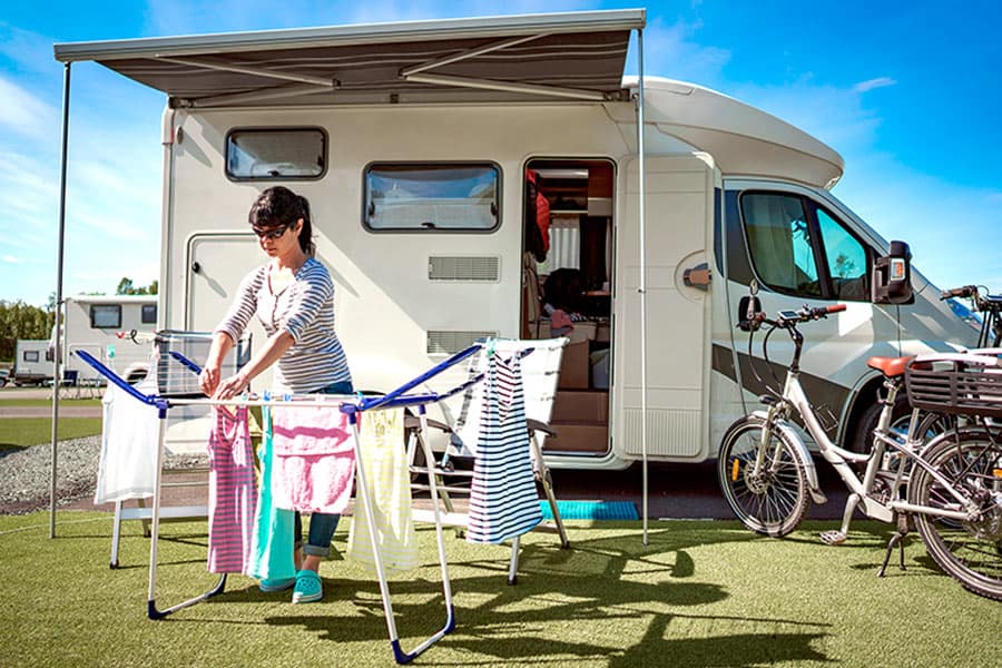 A woman drying clothes on a rack in front of a camper