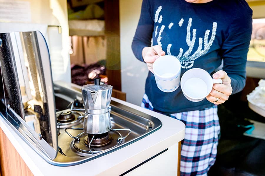 Woman holding mugs waiting for coffee pot to heat up