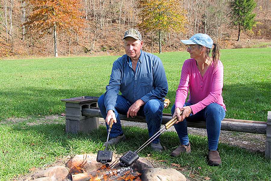 Couple holding pie irons in campfire to made mountain pies