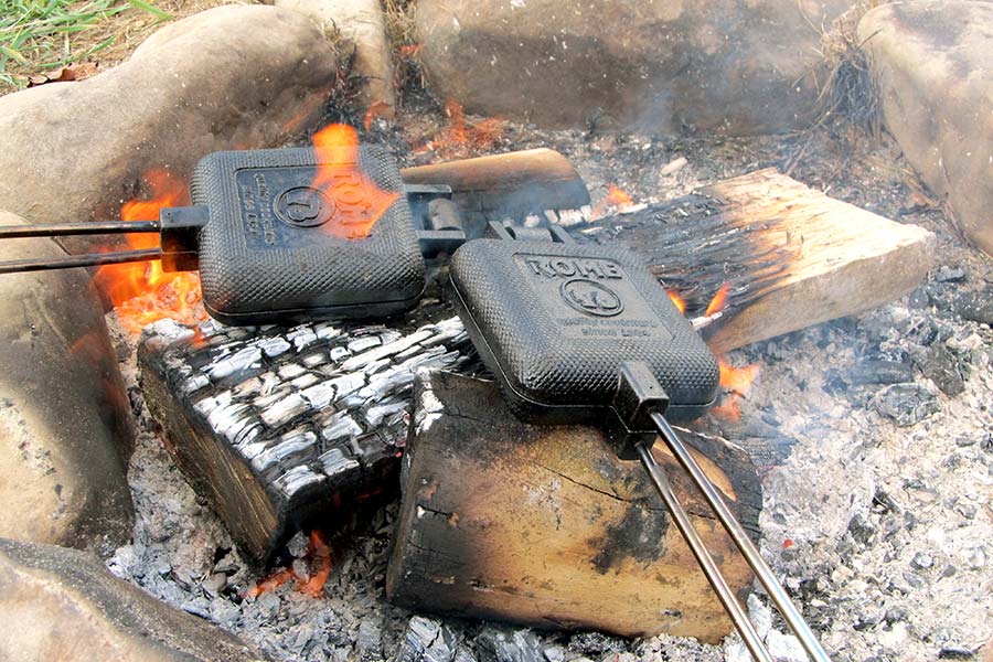Two cast iron pie irons on wood in campfire
