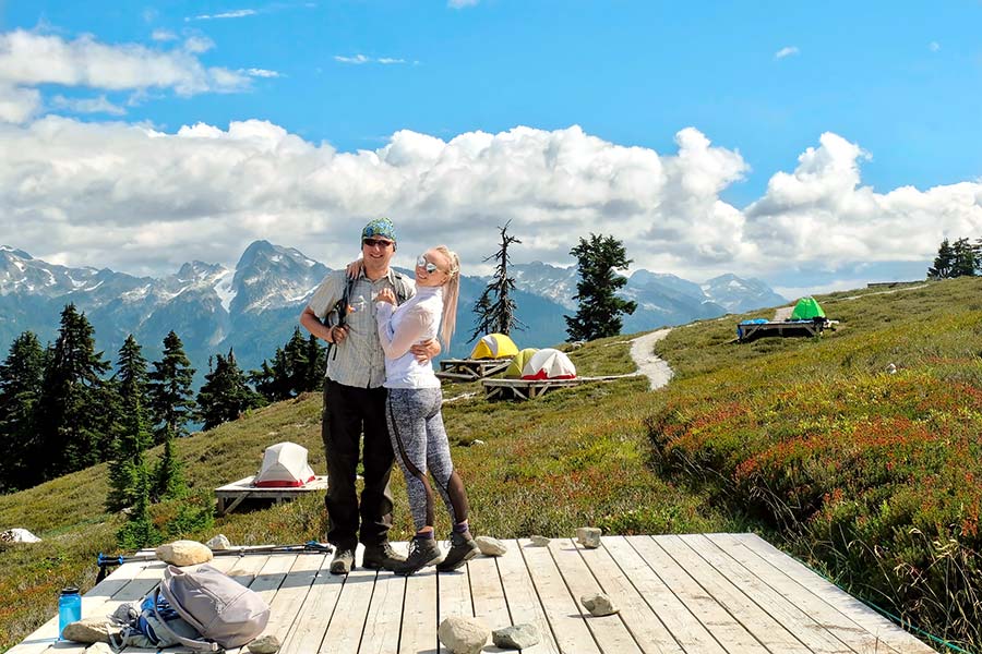Couple standing on wooden tent platform on mountain side