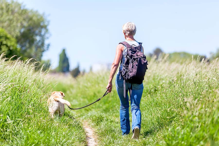 Woman on hiking path through tall grass with her dog